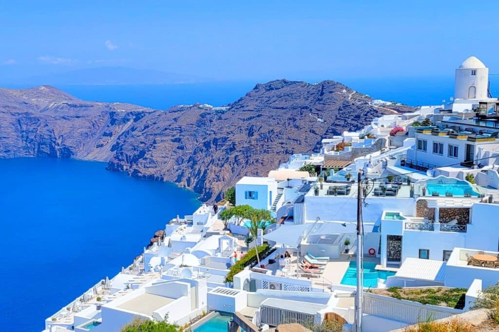 Luxury hotels with private pools line a cliff overlooking the sea in Santorini
